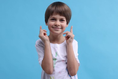 Photo of Portrait of cute boy in t-shirt with handprints drawings on light blue background