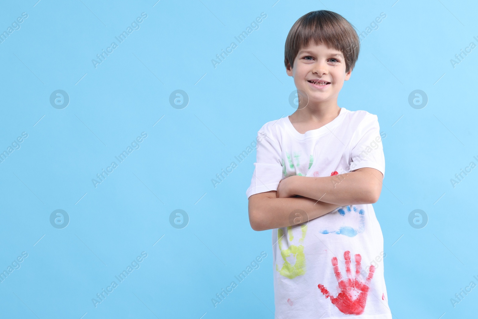 Photo of Portrait of smiling boy in t-shirt with handprints drawings on light blue background. Space for text