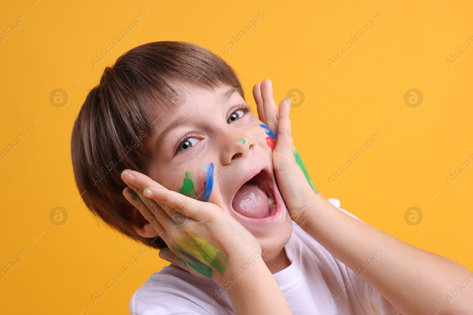 Photo of Portrait of funny boy smeared in paint on orange background