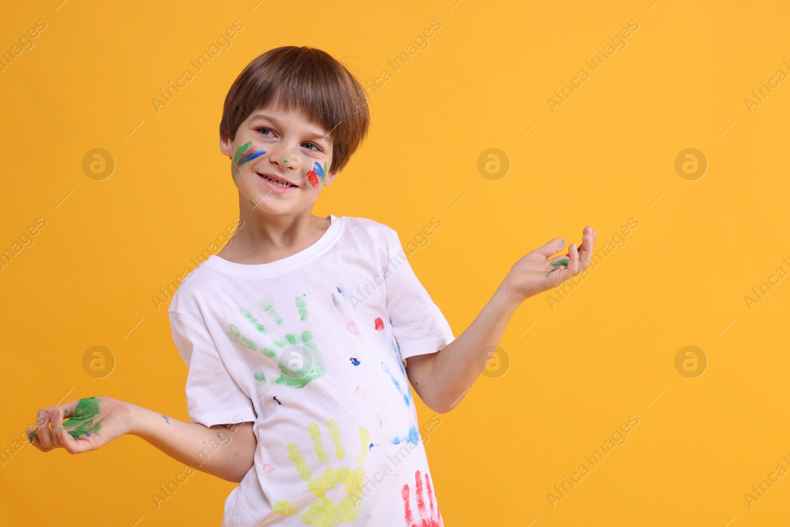 Photo of Portrait of happy boy smeared in paint on orange background