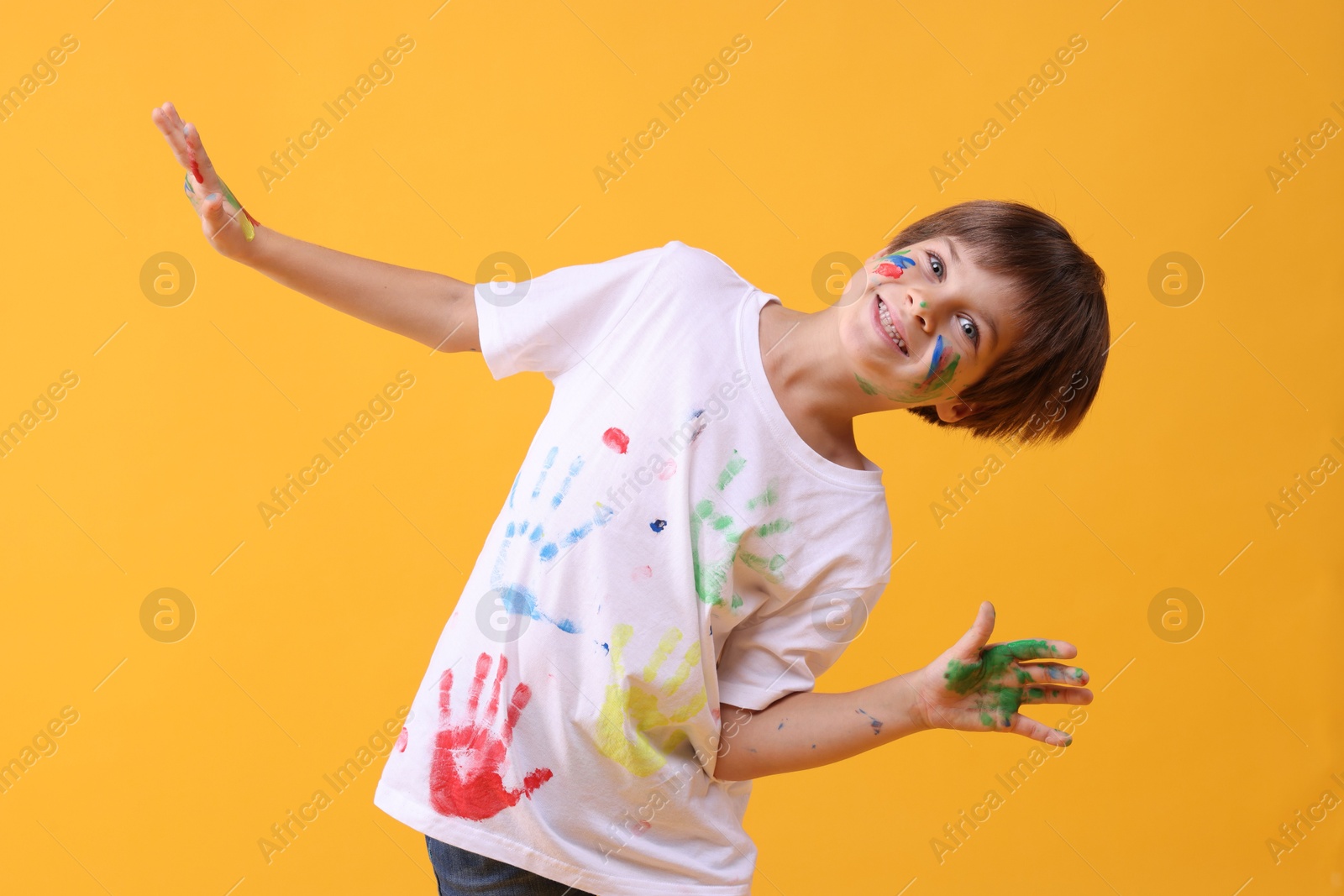 Photo of Portrait of happy boy smeared in paint on orange background