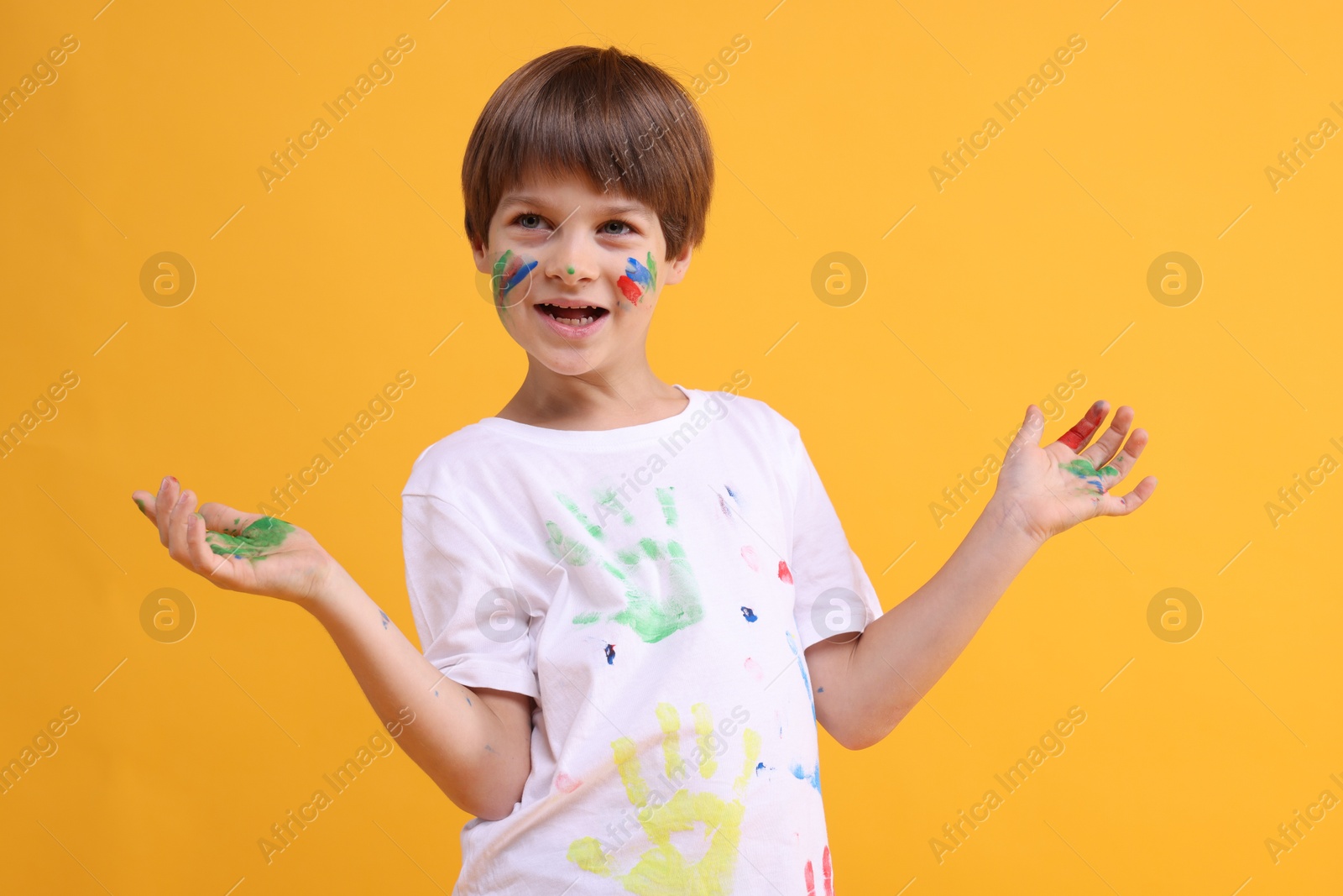 Photo of Portrait of funny boy smeared in paint on orange background