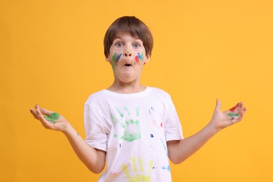 Photo of Portrait of funny boy smeared in paint on orange background