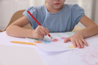 Photo of Girl drawing flowers at white table indoors, closeup