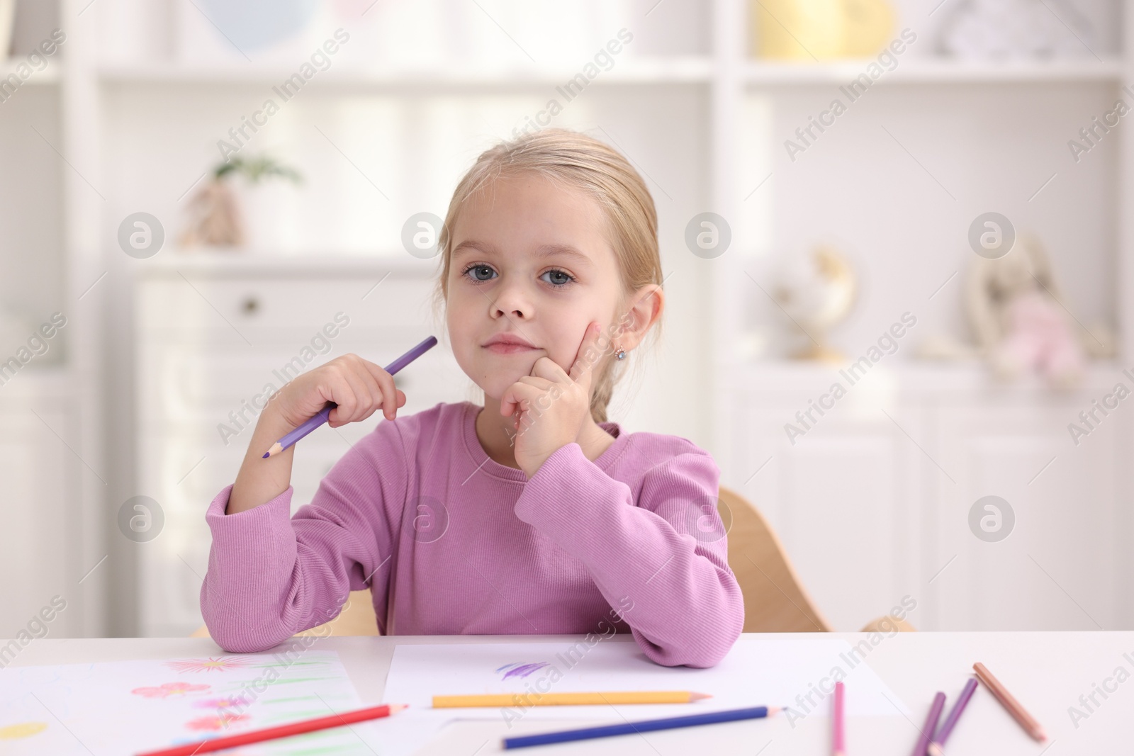 Photo of Cute girl at white table with drawing in kindergarten