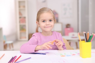 Photo of Cute girl drawing at white table in kindergarten