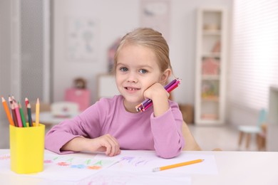 Photo of Smiling girl at white table with drawing and pencils in kindergarten