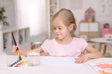 Photo of Cute girl drawing at white table in kindergarten