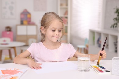 Photo of Cute girl drawing at white table in kindergarten