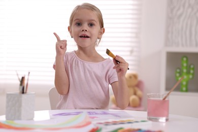 Photo of Cute girl had idea for her drawing at white table in kindergarten