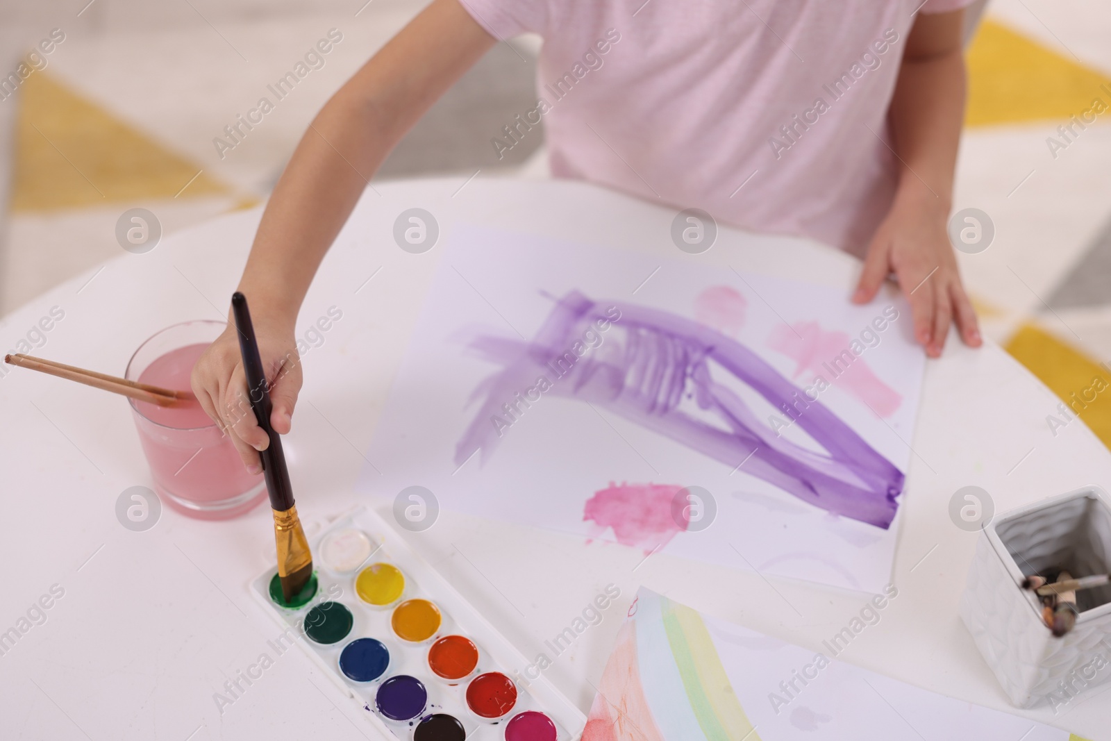 Photo of Girl drawing with paint at white table indoors, closeup