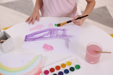 Photo of Girl drawing with paint at white table indoors, closeup