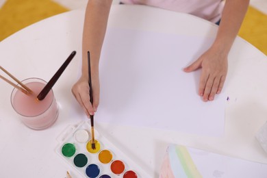 Photo of Girl drawing with paint at white table indoors, above view