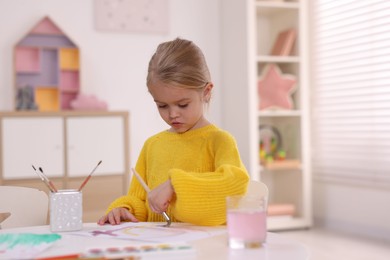 Photo of Cute girl drawing at white table in kindergarten