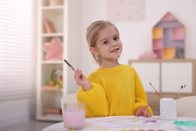 Photo of Smiling girl drawing at white table in kindergarten