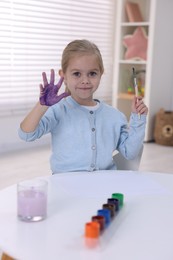 Photo of Cute girl drawing with palm at white table in kindergarten