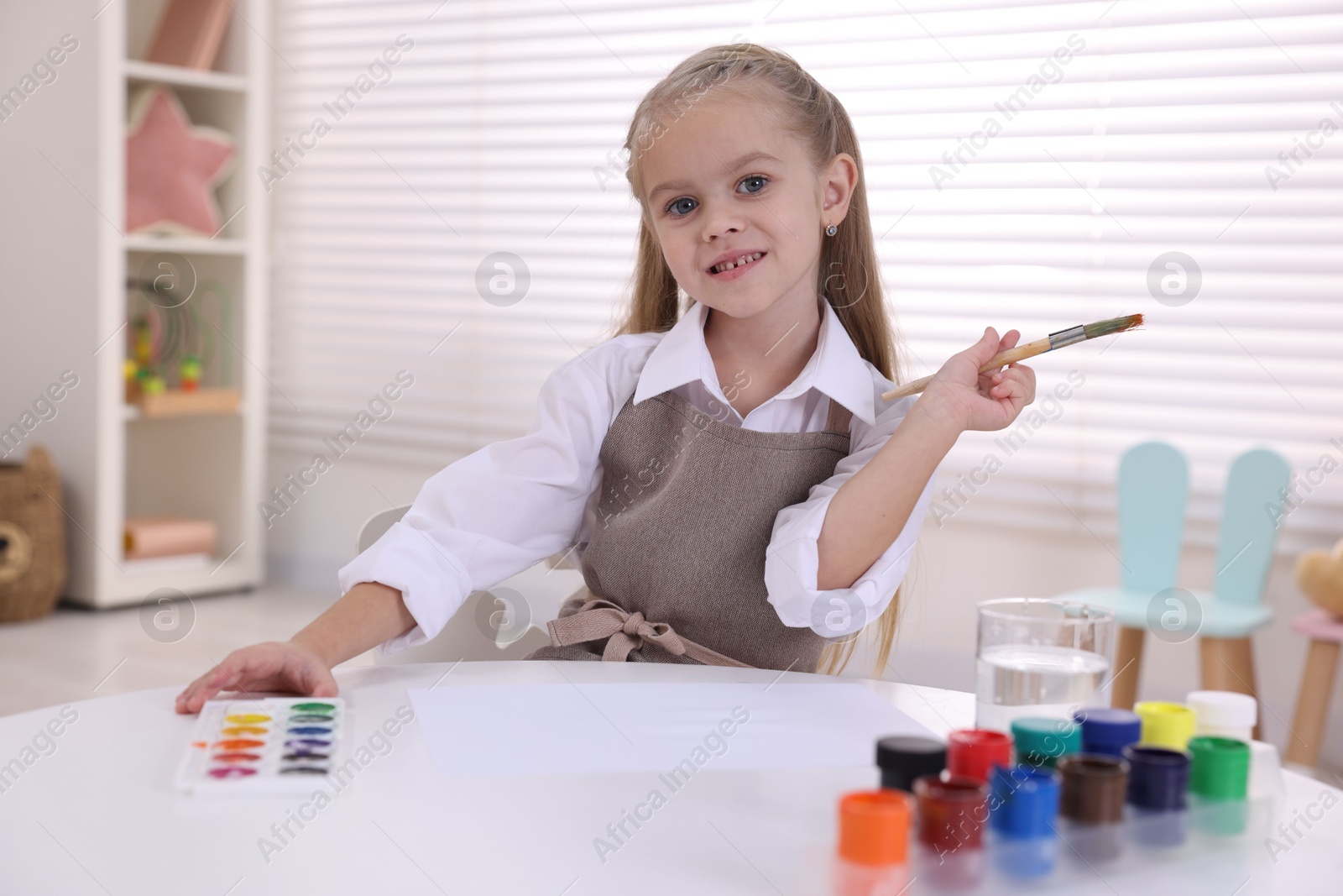 Photo of Smiling girl drawing at white table in kindergarten