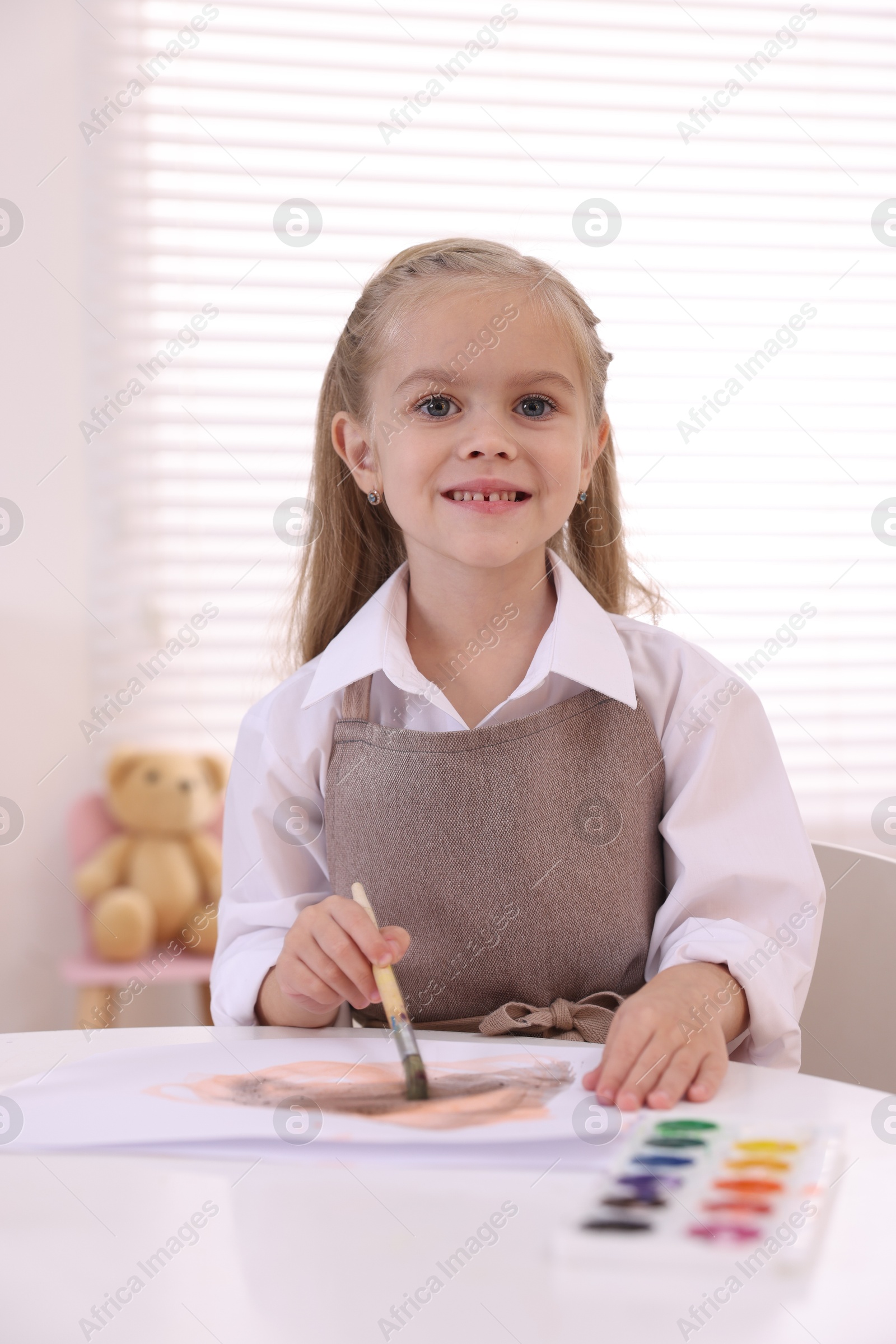 Photo of Smiling girl drawing at white table in kindergarten