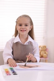 Photo of Smiling girl drawing at white table in kindergarten