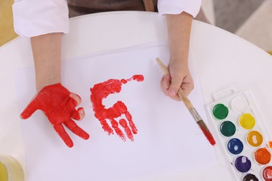 Photo of Girl drawing with palm at white table indoors, top view