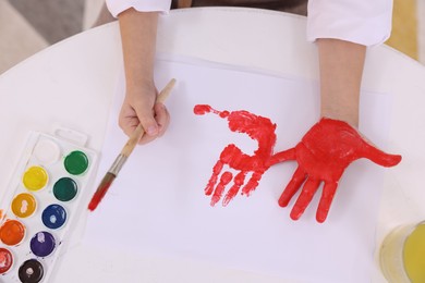 Photo of Girl drawing with palm at white table indoors, top view