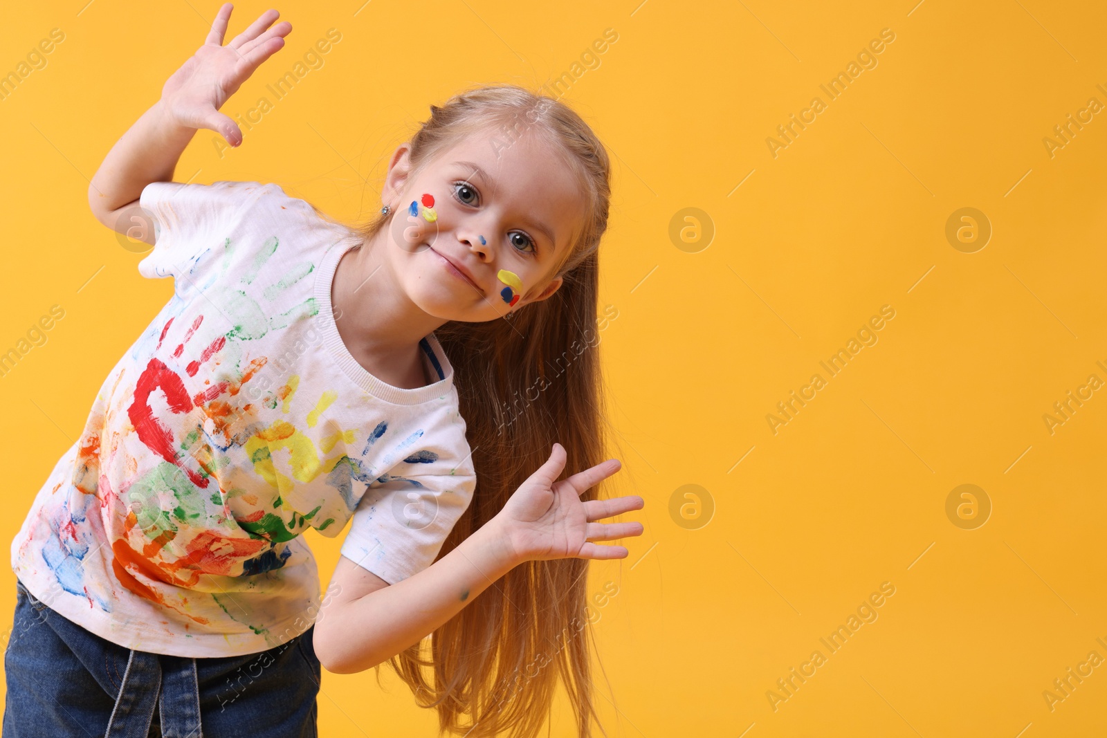 Photo of Portrait of funny girl smeared in paint on orange background. Space for text