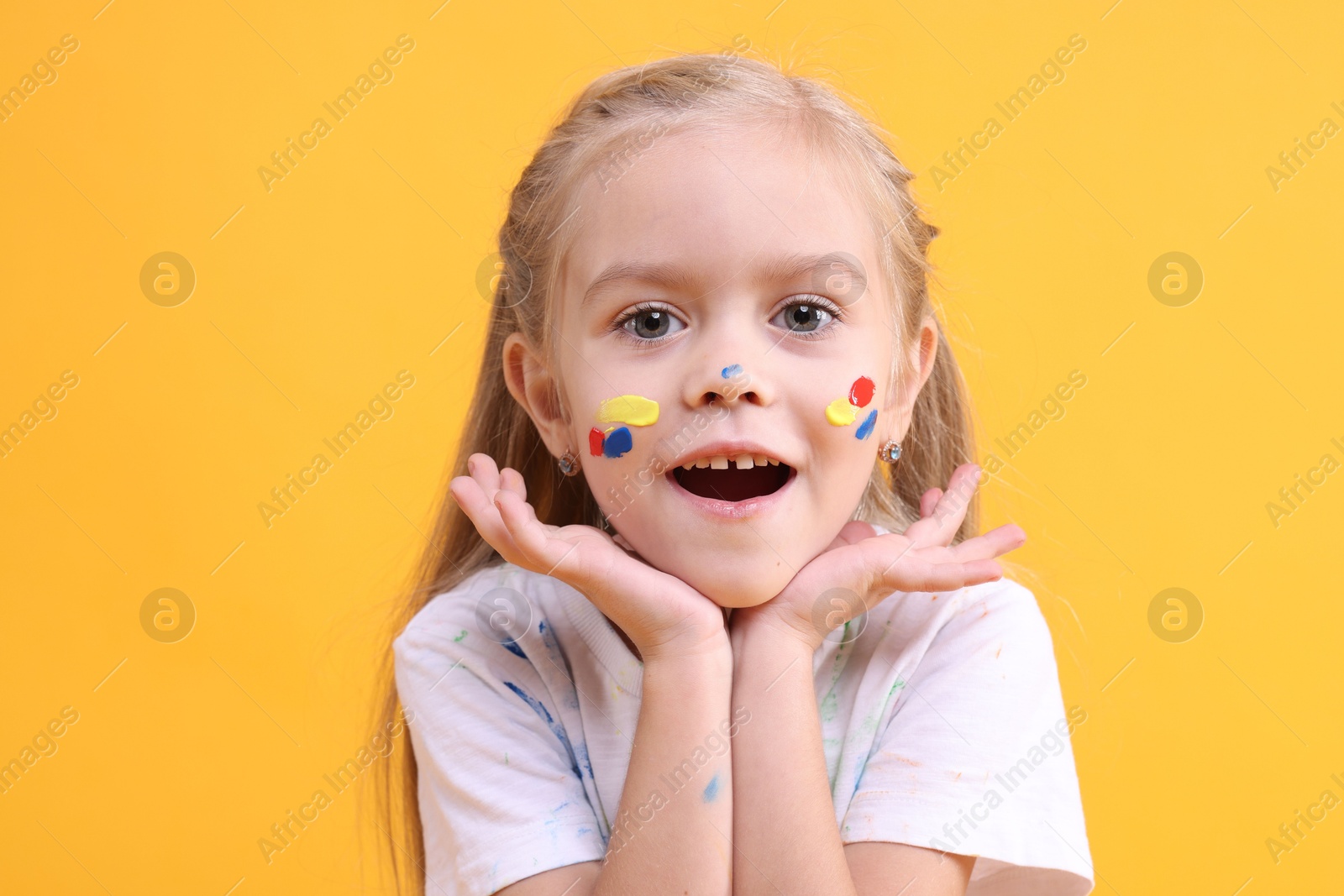 Photo of Portrait of cute girl smeared in paint on orange background. Space for text