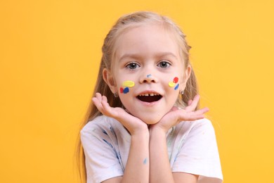 Portrait of cute girl smeared in paint on orange background. Space for text