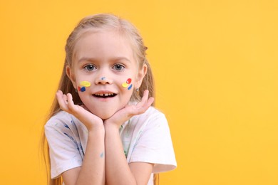 Photo of Portrait of smiling girl smeared in paint on orange background. Space for text