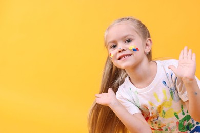 Photo of Portrait of smiling girl smeared in paint on orange background. Space for text