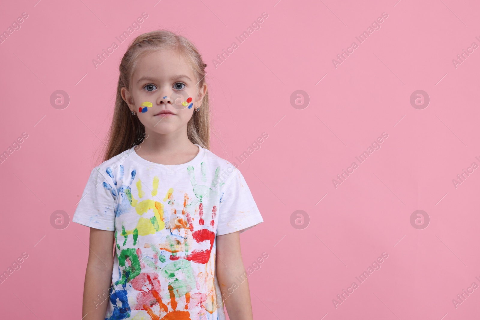 Photo of Portrait of cute girl smeared in paint on pink background. Space for text