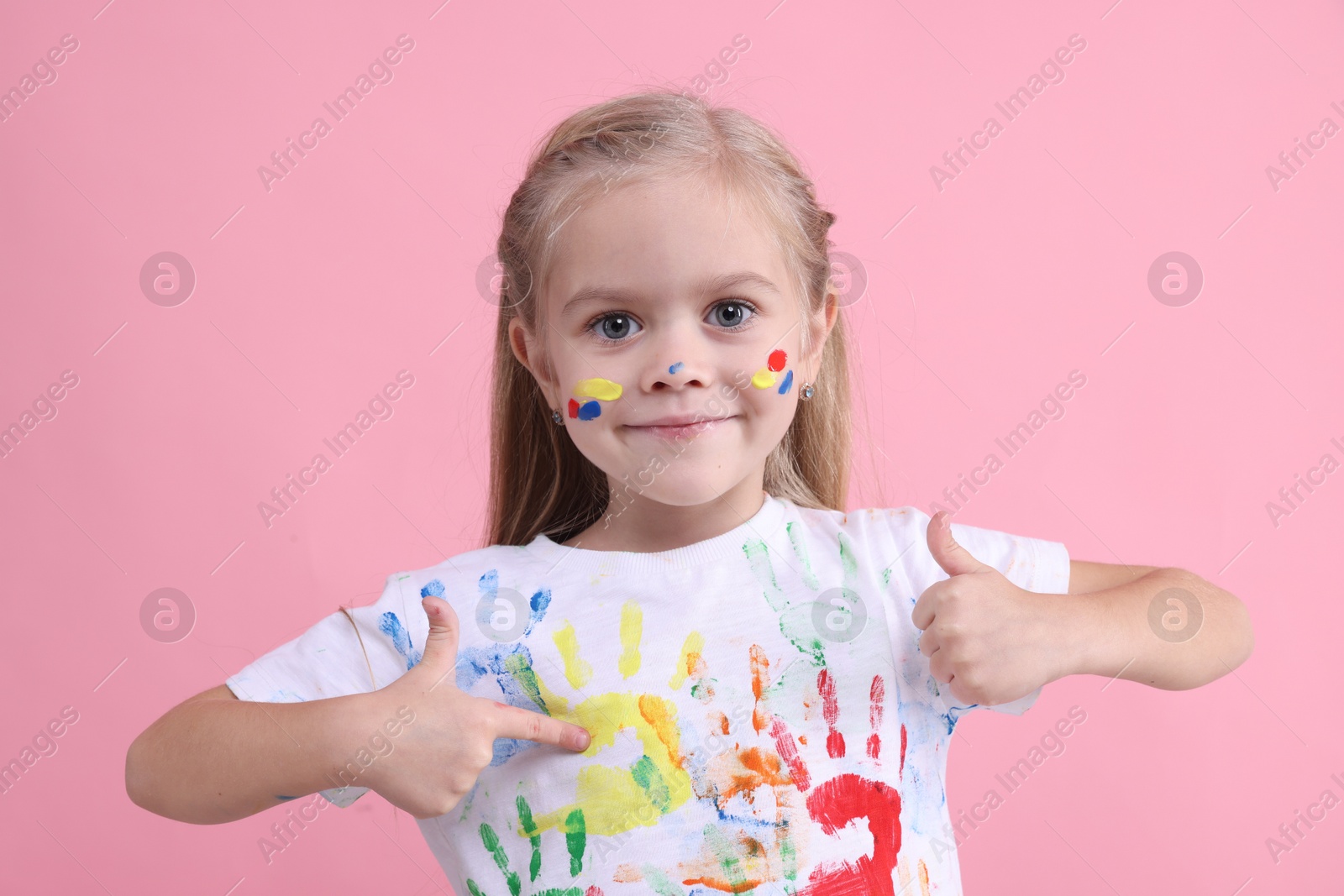 Photo of Portrait of cute girl pointing at her t-shirt with handprints drawings on pink background