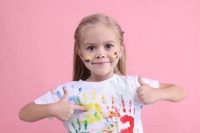 Photo of Portrait of cute girl pointing at her t-shirt with handprints drawings on pink background