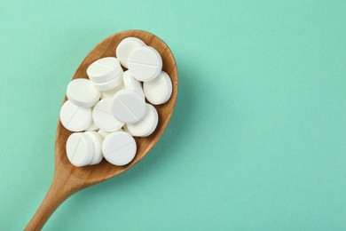 Photo of Antibiotic pills in spoon on turquoise background, top view. Space for text