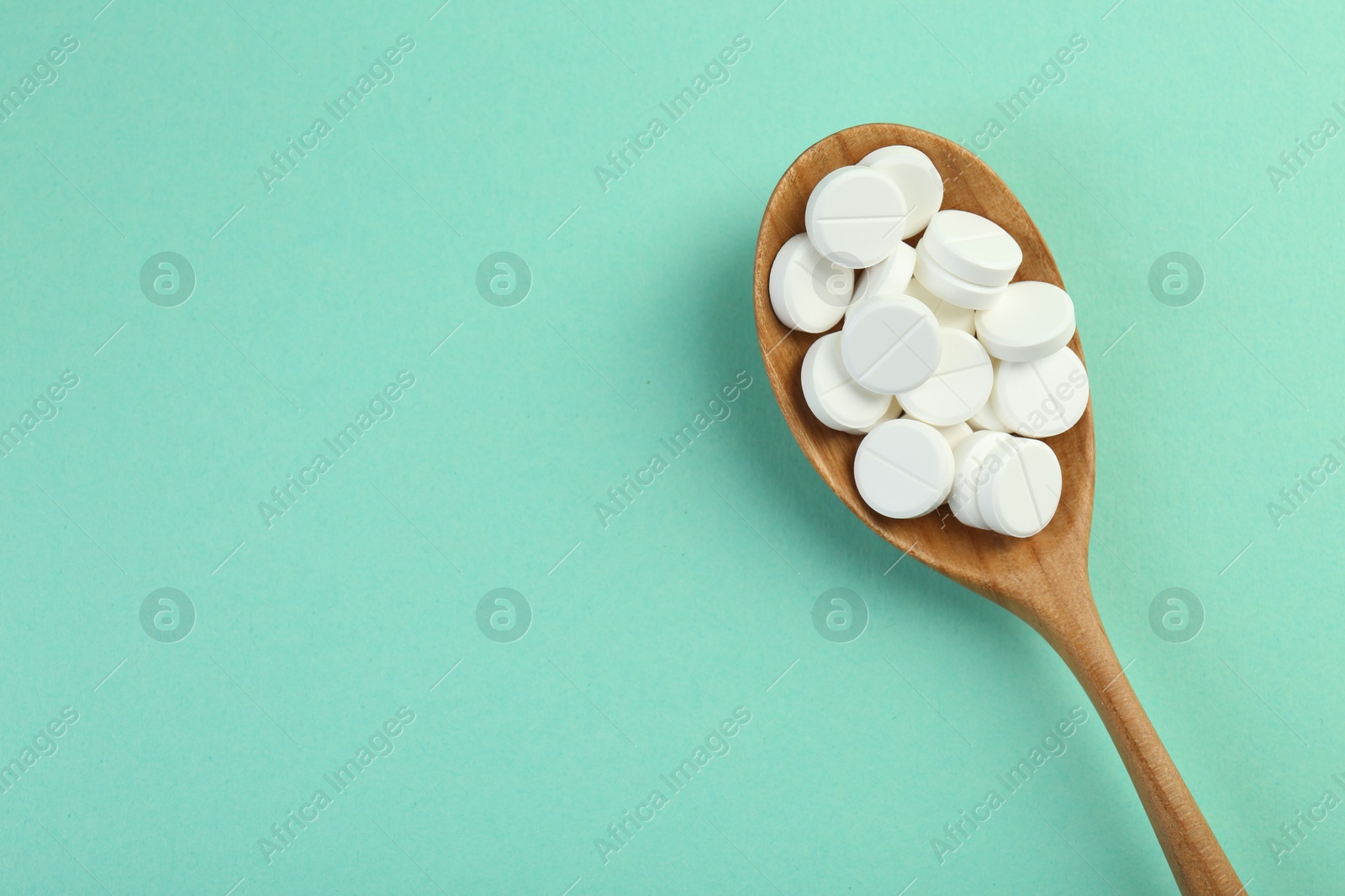 Photo of Antibiotic pills in spoon on turquoise background, top view. Space for text