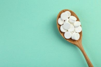 Photo of Antibiotic pills in spoon on turquoise background, top view. Space for text