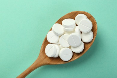 Photo of Antibiotic pills in spoon on turquoise background, top view