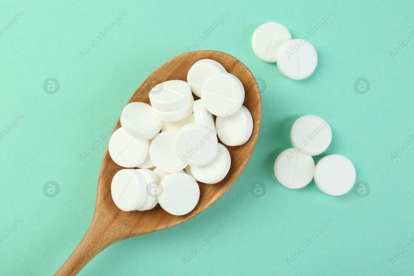 Photo of Antibiotic pills in spoon on turquoise background, top view