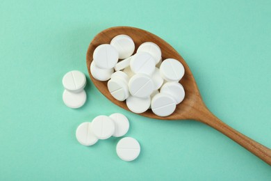 Photo of Antibiotic pills in spoon on turquoise background, top view