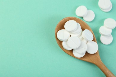 Photo of Antibiotic pills in spoon on turquoise background, top view. Space for text