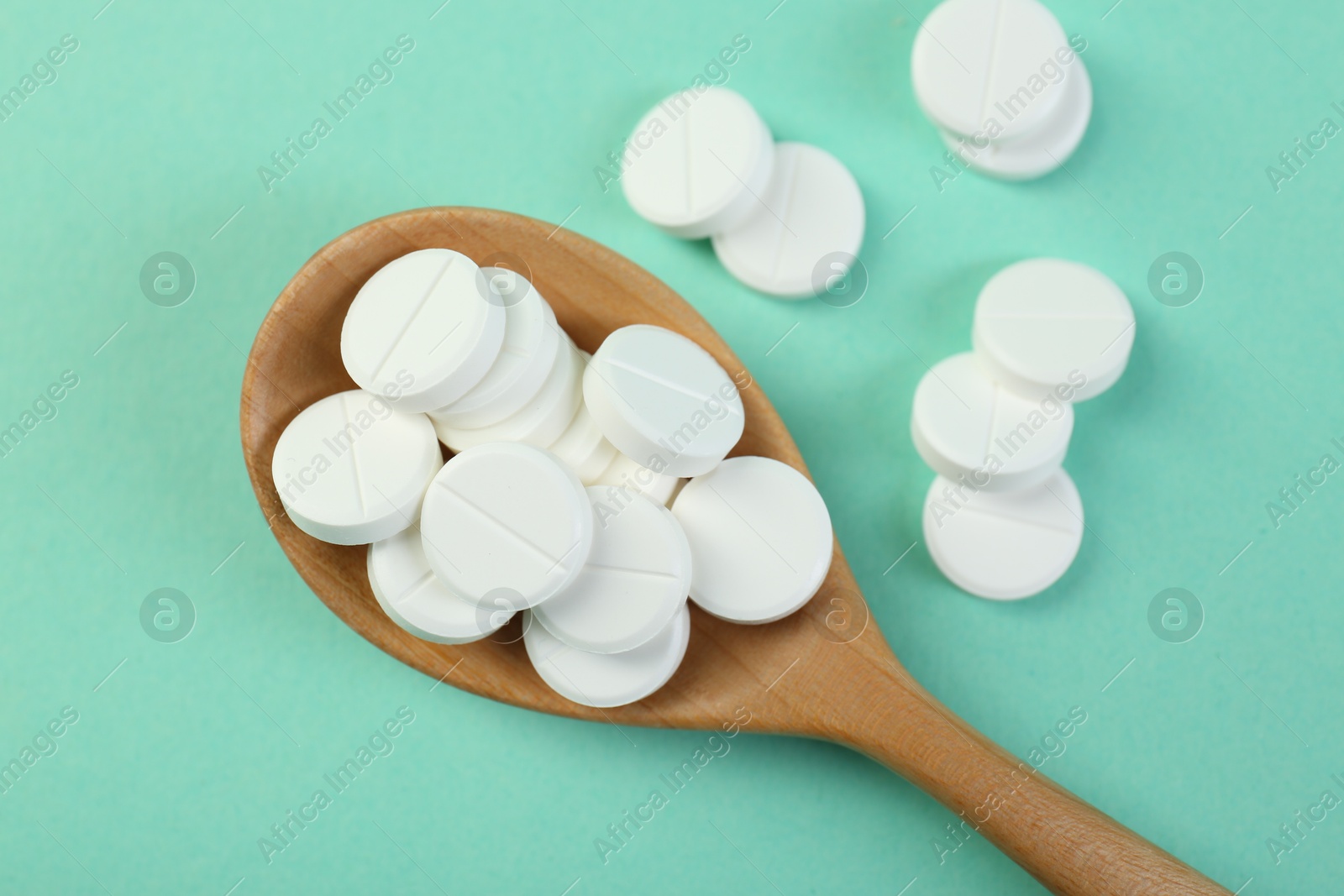 Photo of Antibiotic pills in spoon on turquoise background, top view