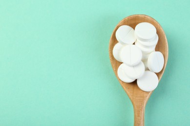 Photo of Antibiotic pills in spoon on turquoise background, top view. Space for text