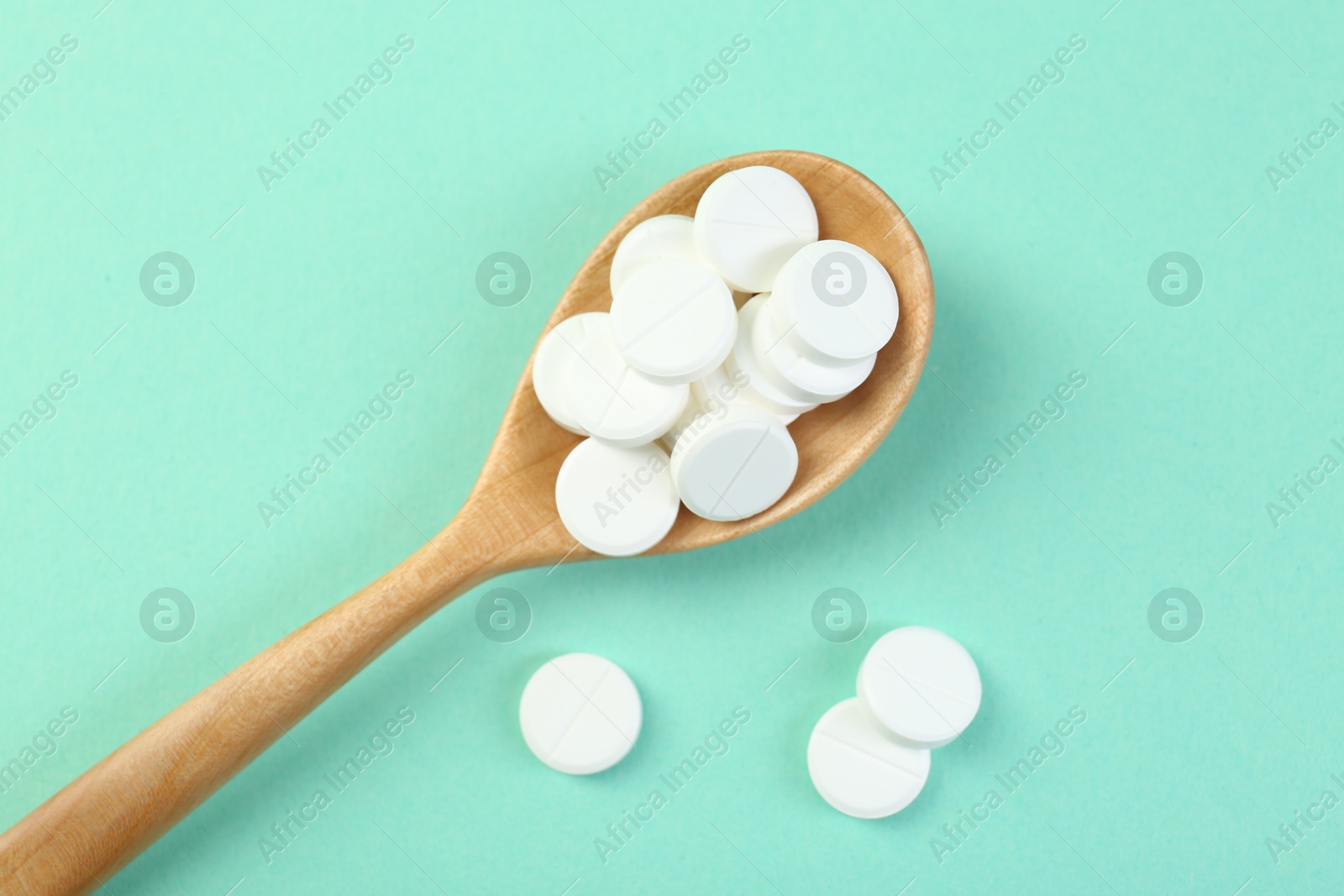 Photo of Antibiotic pills in spoon on turquoise background, top view