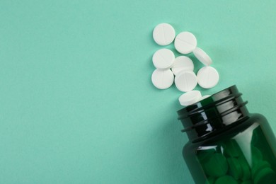 Photo of Medical bottle with antibiotic pills on turquoise background, top view. Space for text