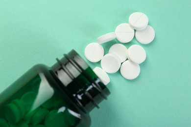 Photo of Medical bottle with antibiotic pills on turquoise background, top view