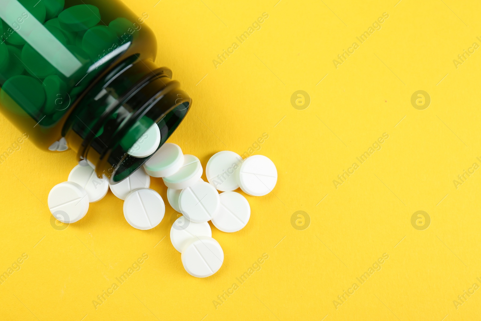 Photo of Medical bottle with antibiotic pills on yellow background, top view. Space for text