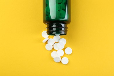 Photo of Medical bottle with antibiotic pills on yellow background, top view