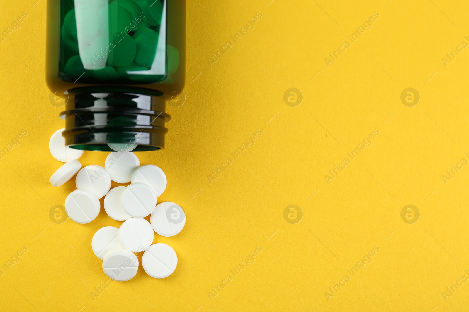 Photo of Medical bottle with antibiotic pills on yellow background, top view. Space for text