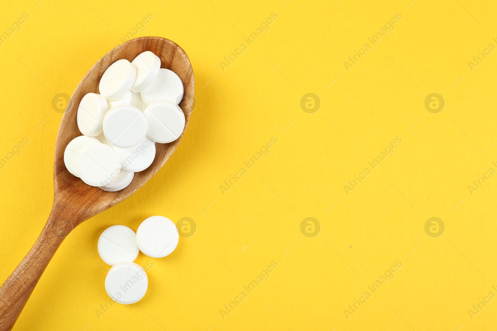 Photo of Antibiotic pills in spoon on yellow background, top view. Space for text