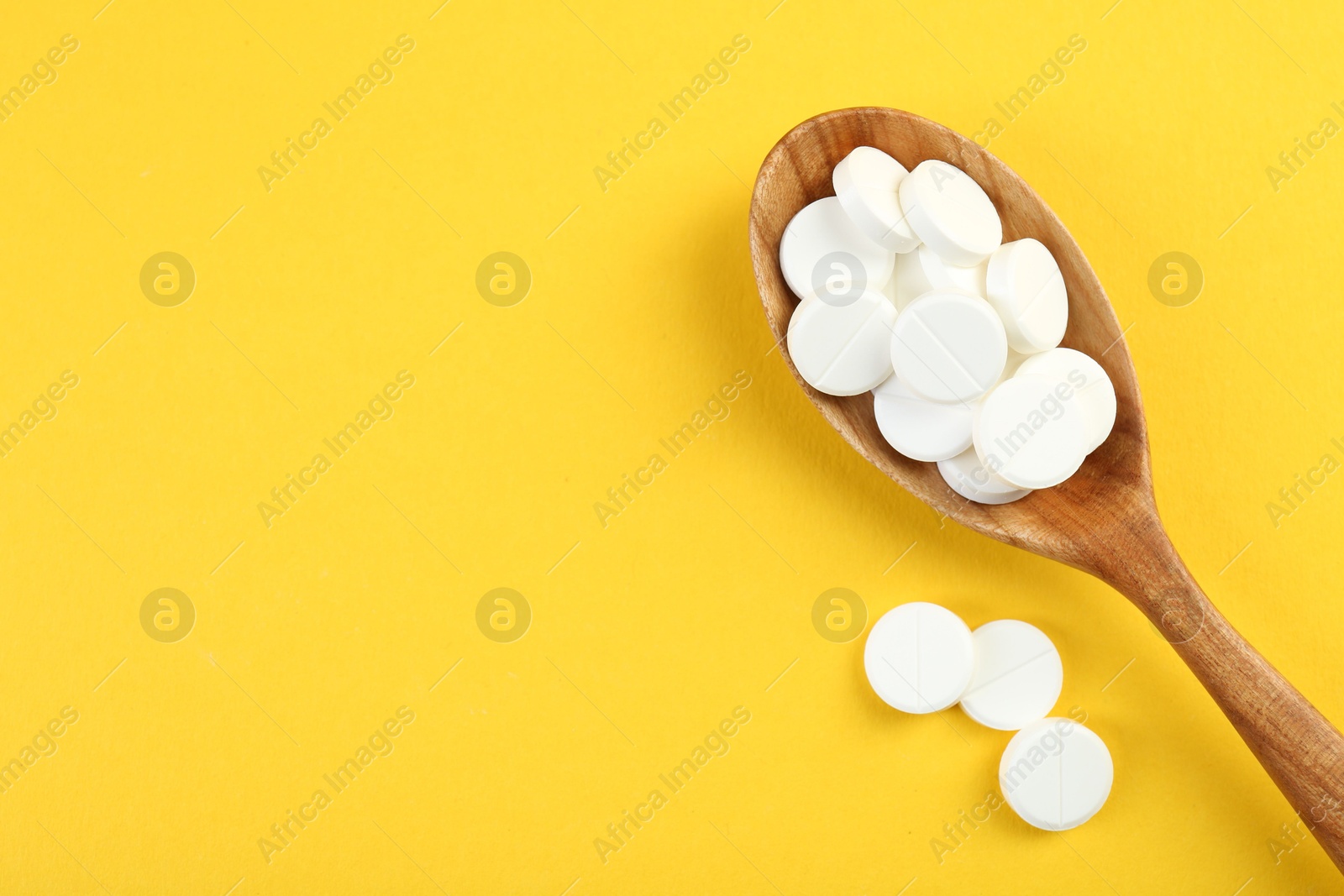 Photo of Antibiotic pills in spoon on yellow background, top view. Space for text